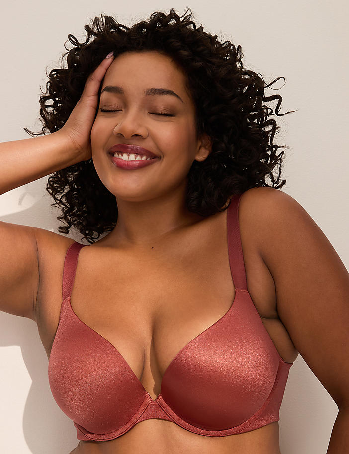 A smiling woman with curly dark hair and a rose-colored bra is posed against a plain, light-colored background.
