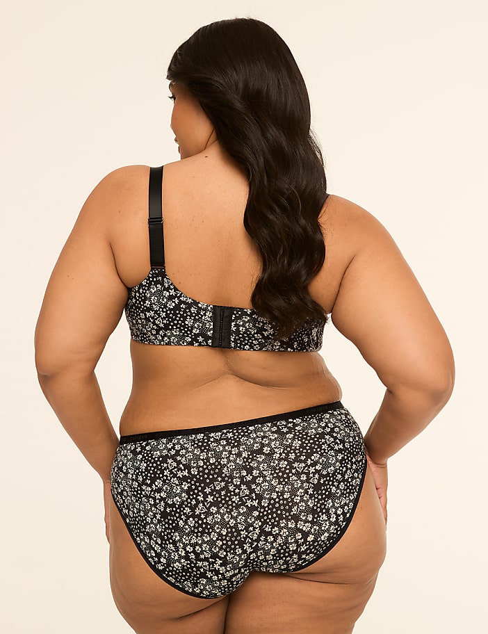 A woman in a floral bra and underwear stands against a plain, light-colored background.