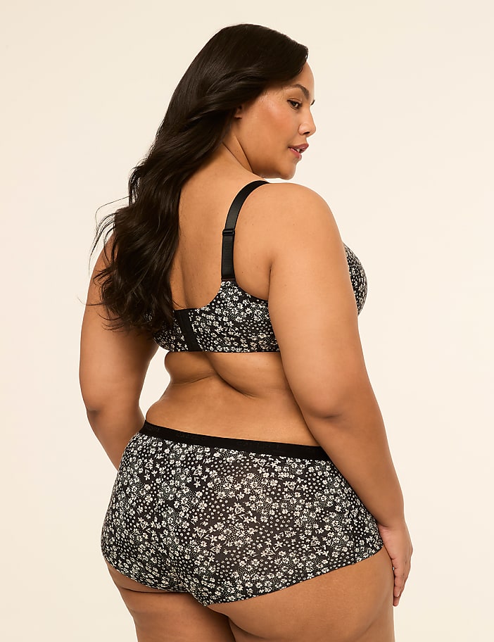A woman in a floral bra and shorts stands against a plain, light-colored background.