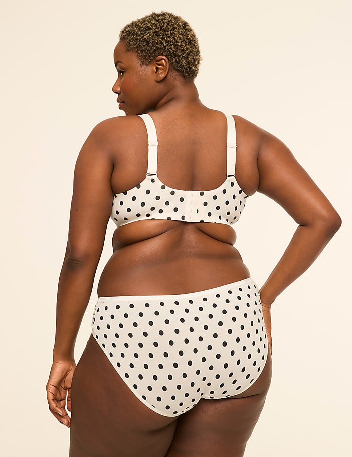 A woman in a polka dot bra and underwear stands against a plain, light-colored background.
