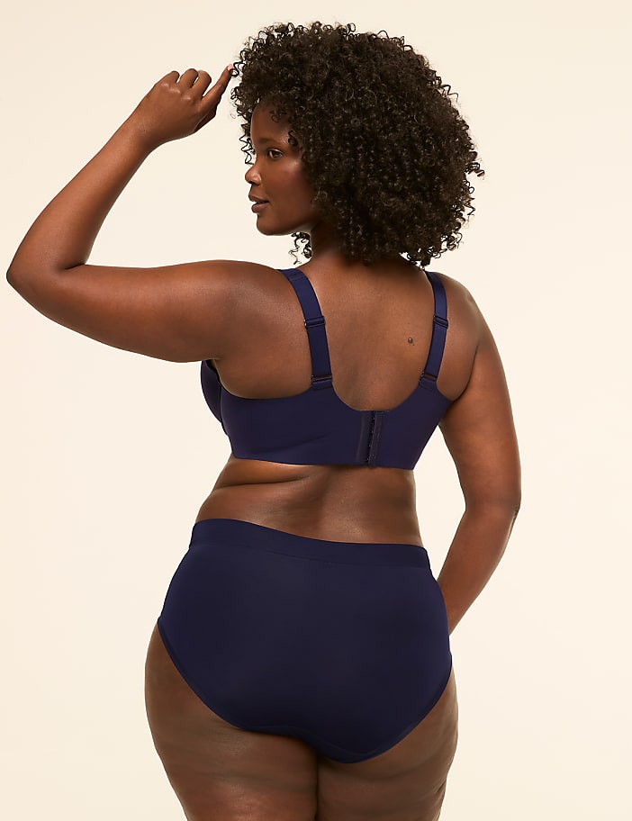 A woman in navy blue lingerie stands with her back to the viewer against a plain, light-colored background.