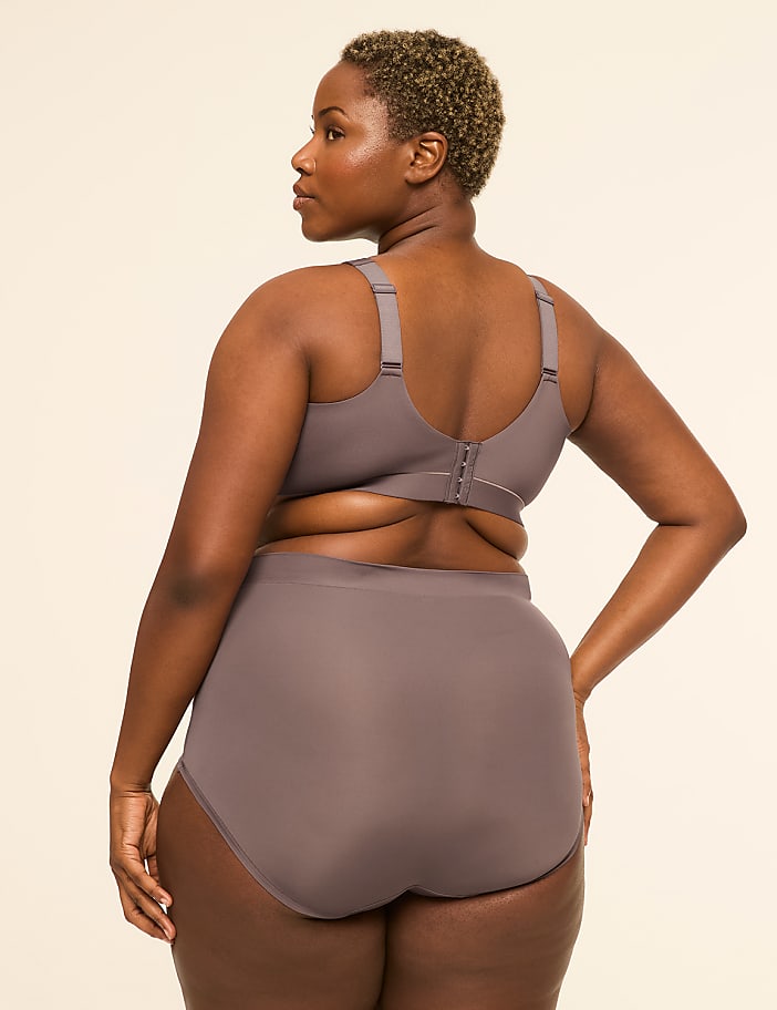 A woman in a grey bra and underwear stands against a plain beige background.