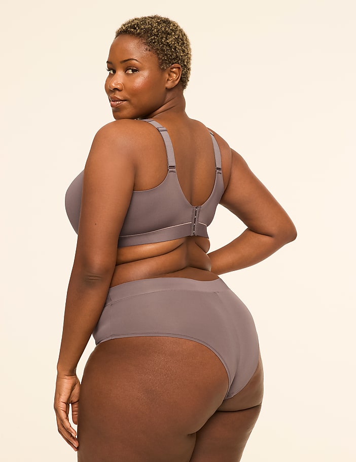 A woman in a grey bra and underwear stands against a plain, light-colored background.