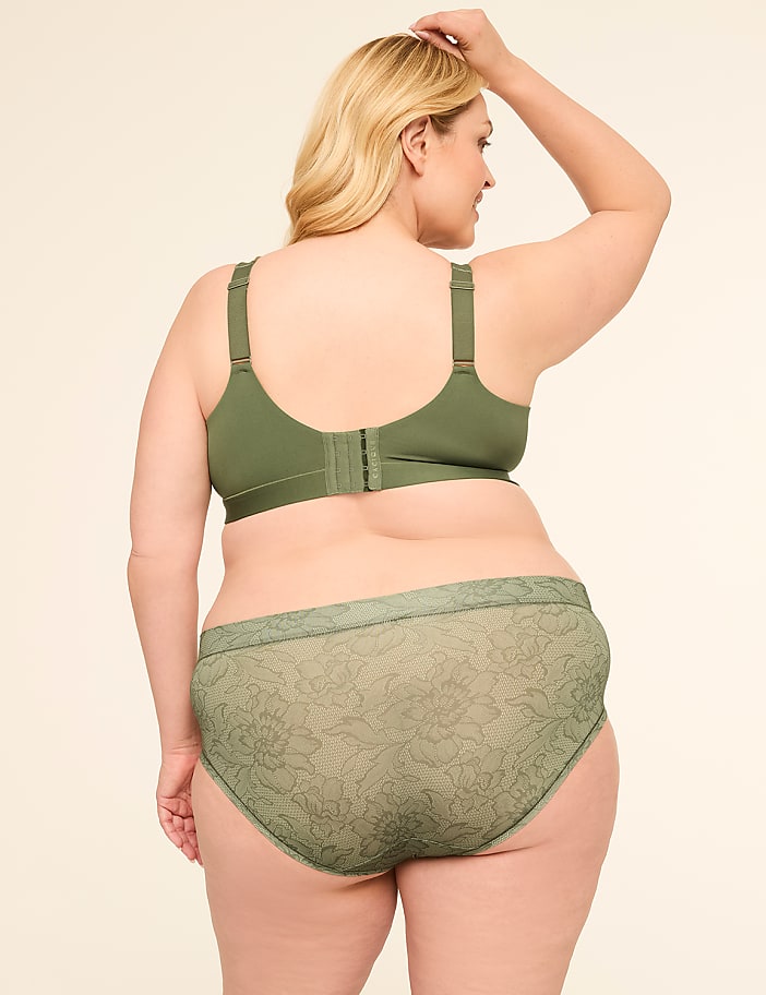 A woman in a green bra and matching patterned underwear stands with her back to the viewer against a plain, light background.