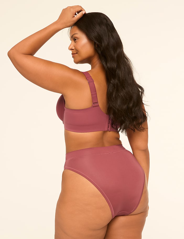 A woman in a mauve bra and high-waisted underwear stands against a plain, light-colored background.