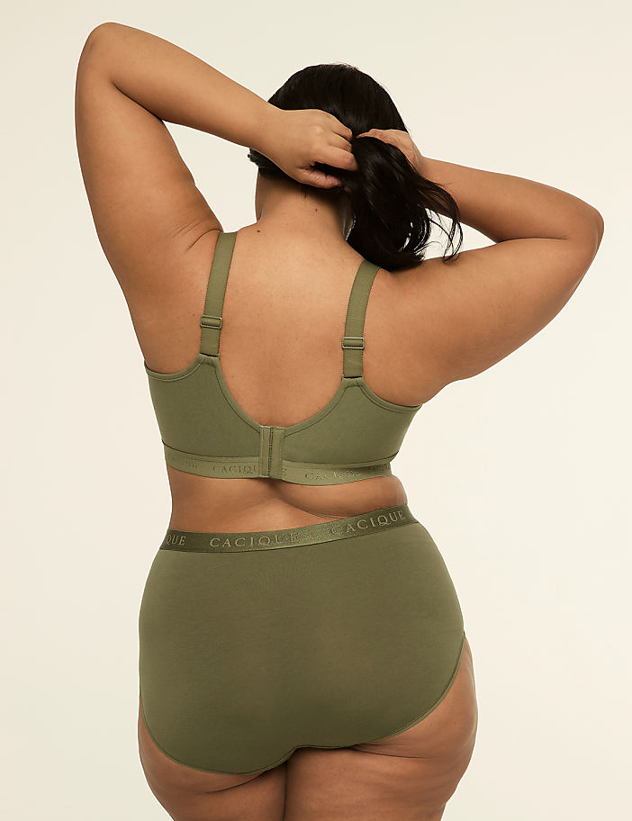 A woman in olive green lingerie stands with her back to the viewer against a plain, light background.