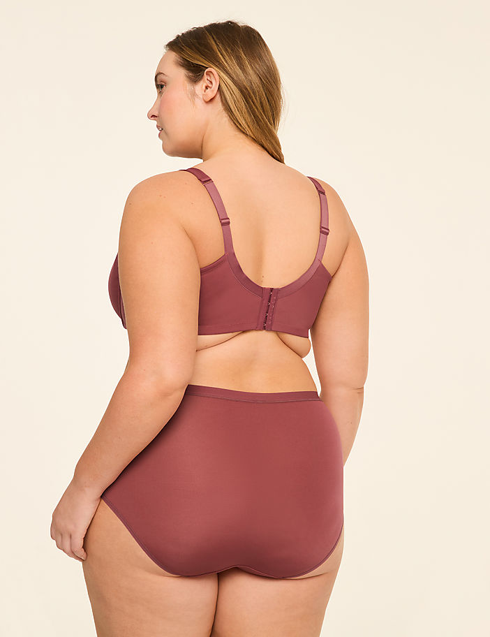 A woman in a mauve bra and matching high-waisted briefs stands against a plain, light-colored background.