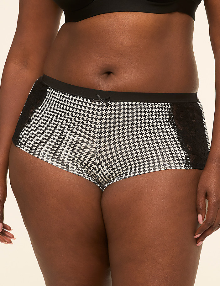 A woman in houndstooth patterned boy shorts with black lace accents stands against a plain background.