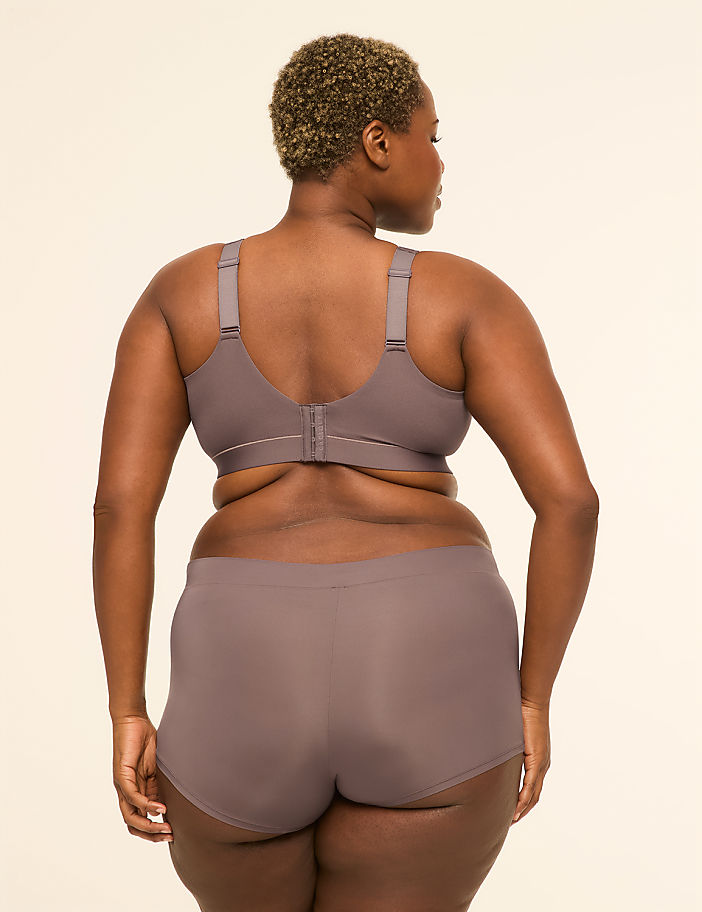 A woman in a grey bra and underwear stands facing away from the camera against a plain, light background.