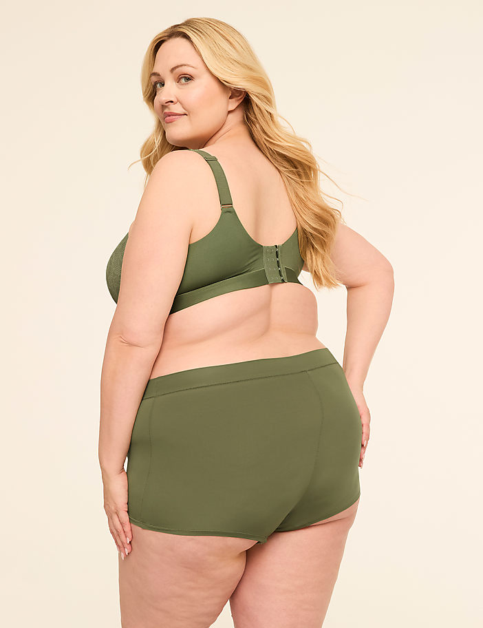 A blonde woman in olive green lingerie stands against a plain, light-colored background.