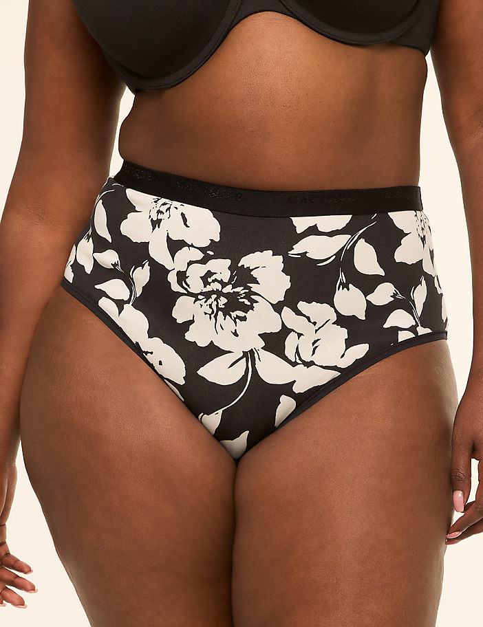 A person models high-waisted black underwear with a bold white floral pattern against a plain background.