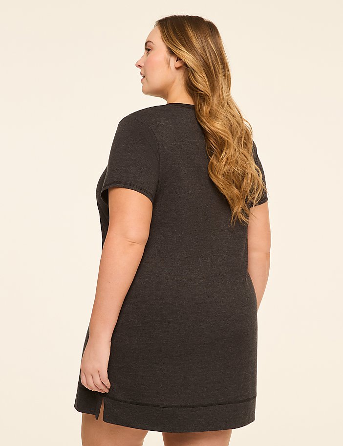 A woman in a dark grey t-shirt dress stands against a plain, light beige background.