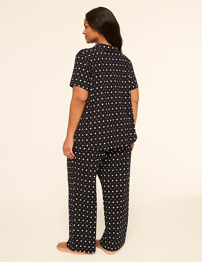 A woman in black pajamas with a white star pattern stands against a plain, light-colored background.