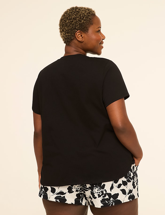 A woman in a black t-shirt and floral shorts stands against a plain, light-colored background.