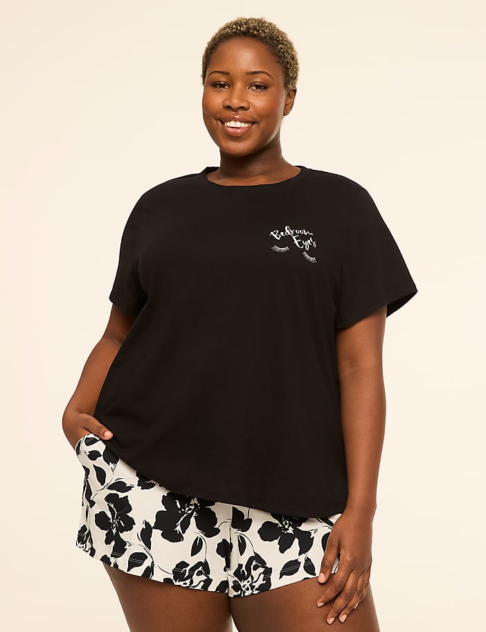 A smiling woman in a black t-shirt and floral shorts stands against a plain, light-colored background.