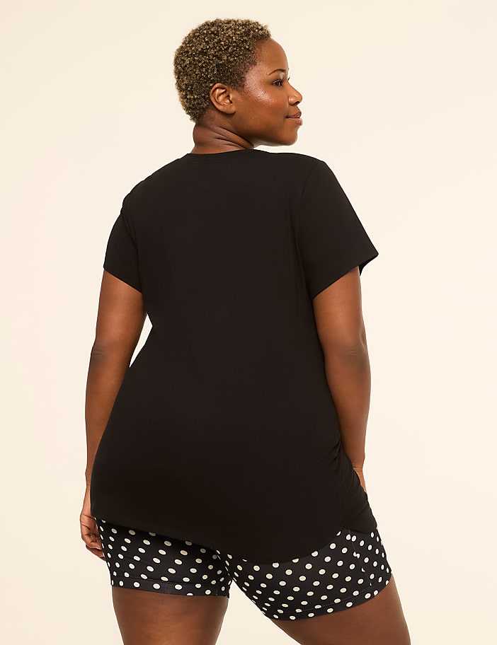 A woman in a black t-shirt and polka dot shorts stands against a plain, light-colored background.