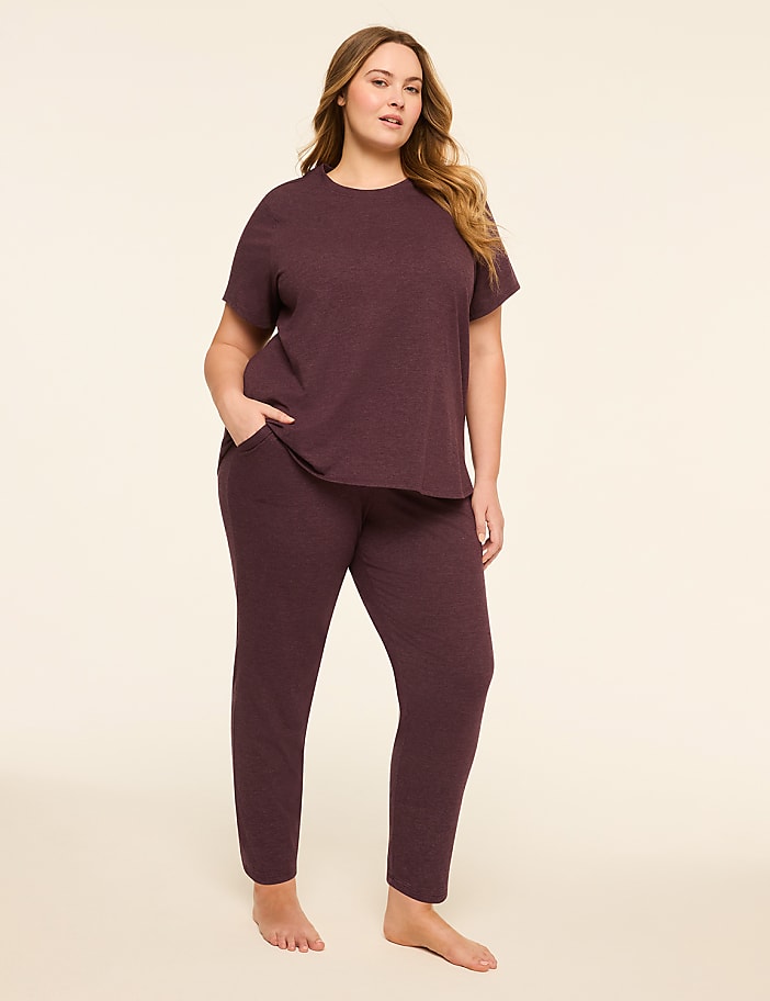 A woman in a burgundy loungewear set stands with her hand in her pocket against a plain, light-colored background.