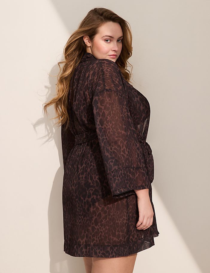A woman in a sheer leopard-print robe stands against a plain, light-colored wall with soft shadows.