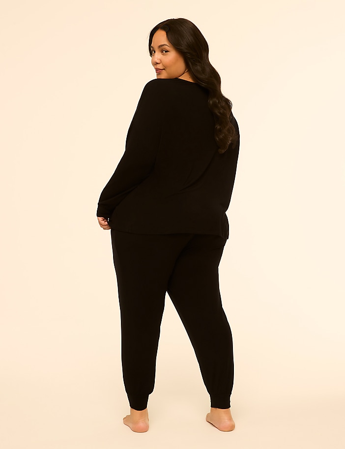 A woman in a black loungewear set stands against a plain, light-colored background.
