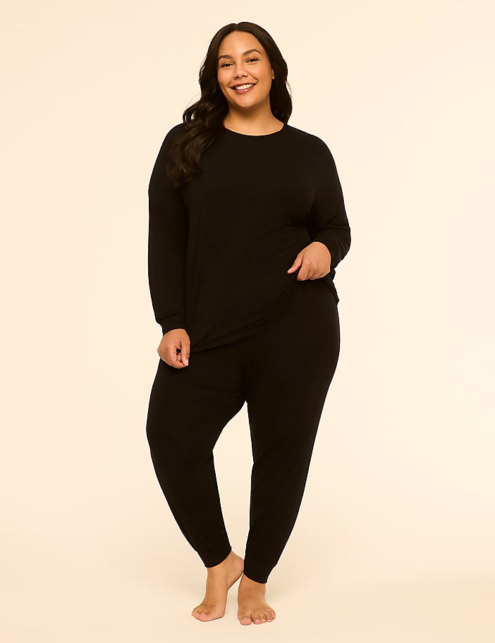 A smiling woman in a black loungewear set stands against a plain, light-colored background.
