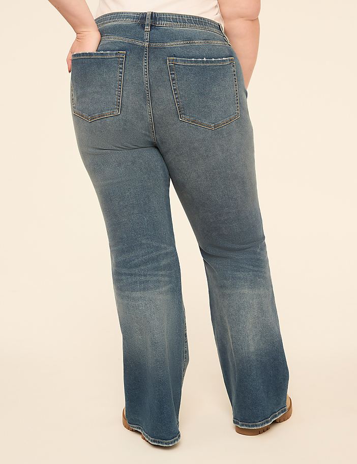 A person wearing flared denim jeans stands against a plain, light-colored background.