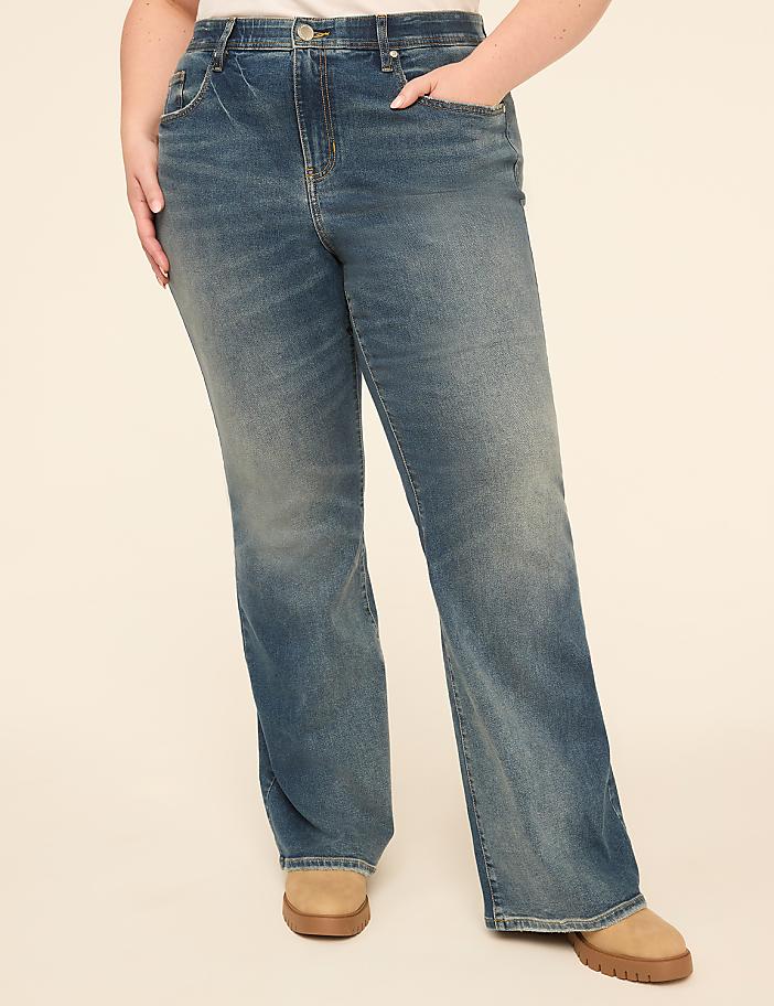A person wearing flared blue jeans and tan boots stands against a plain, light-colored background.