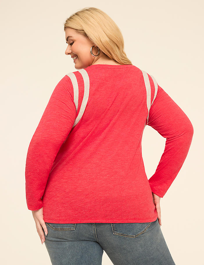 A woman in a red long-sleeved shirt and jeans stands against a plain, light-colored background.