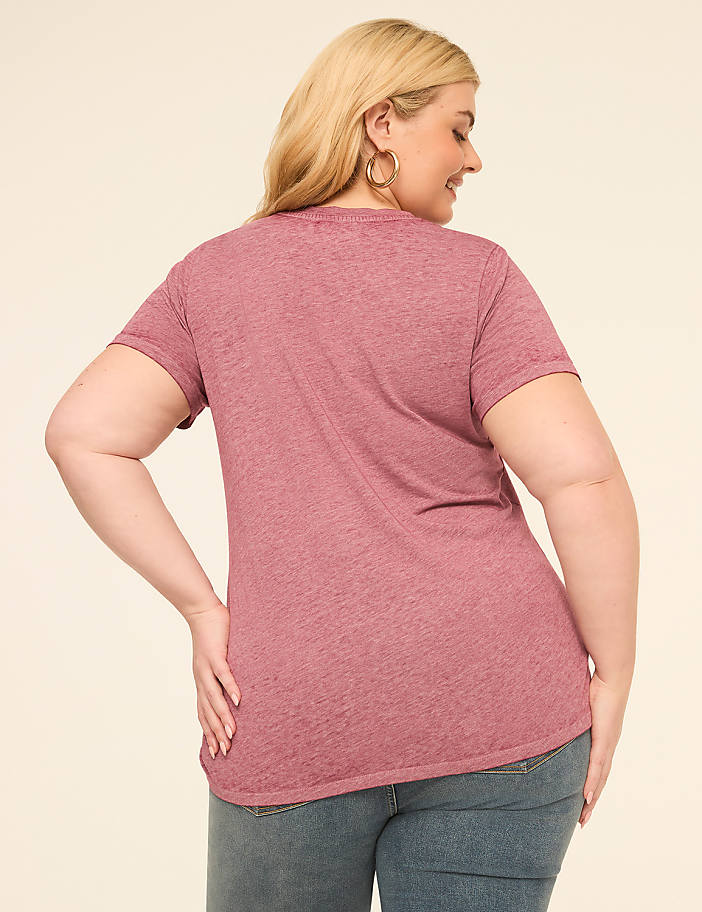 A woman in a pink t-shirt and jeans stands against a plain, light-colored background.
