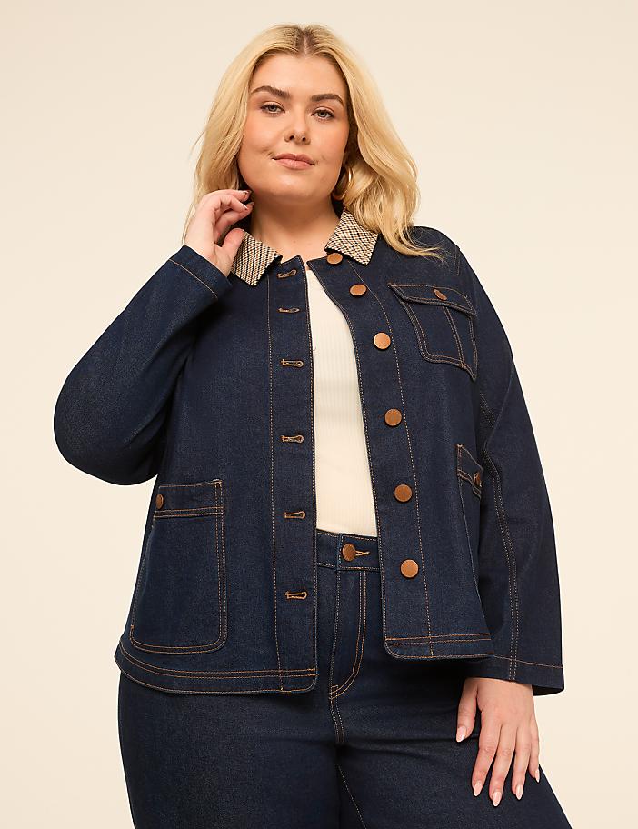 A plus-size woman in a denim jacket stands against a plain, light-colored background.
