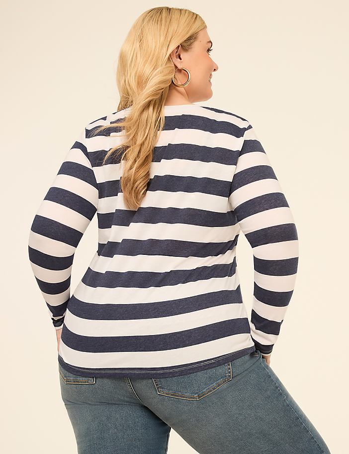 A woman in a striped shirt and jeans stands against a plain, light-colored background.