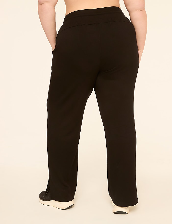 A person wearing black sweatpants and sneakers stands against a plain, light-colored background.