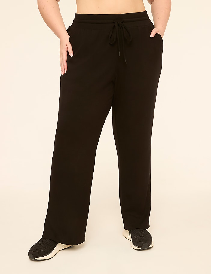 A person wearing black sweatpants with pockets and a drawstring stands against a plain, light-colored background.