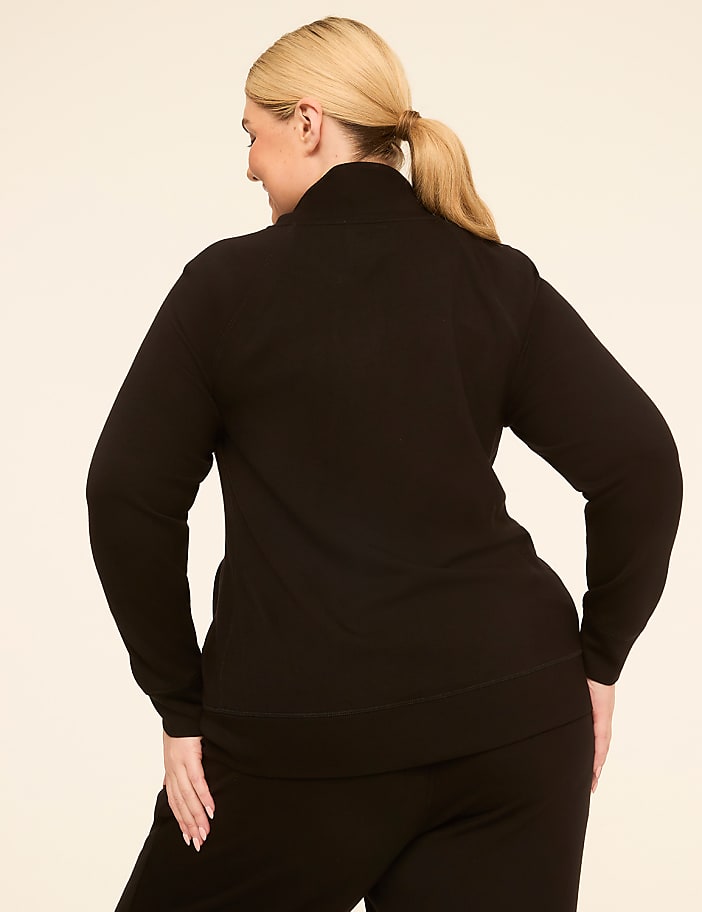 A woman in a black zip-up jacket and pants stands against a plain, light-colored background.