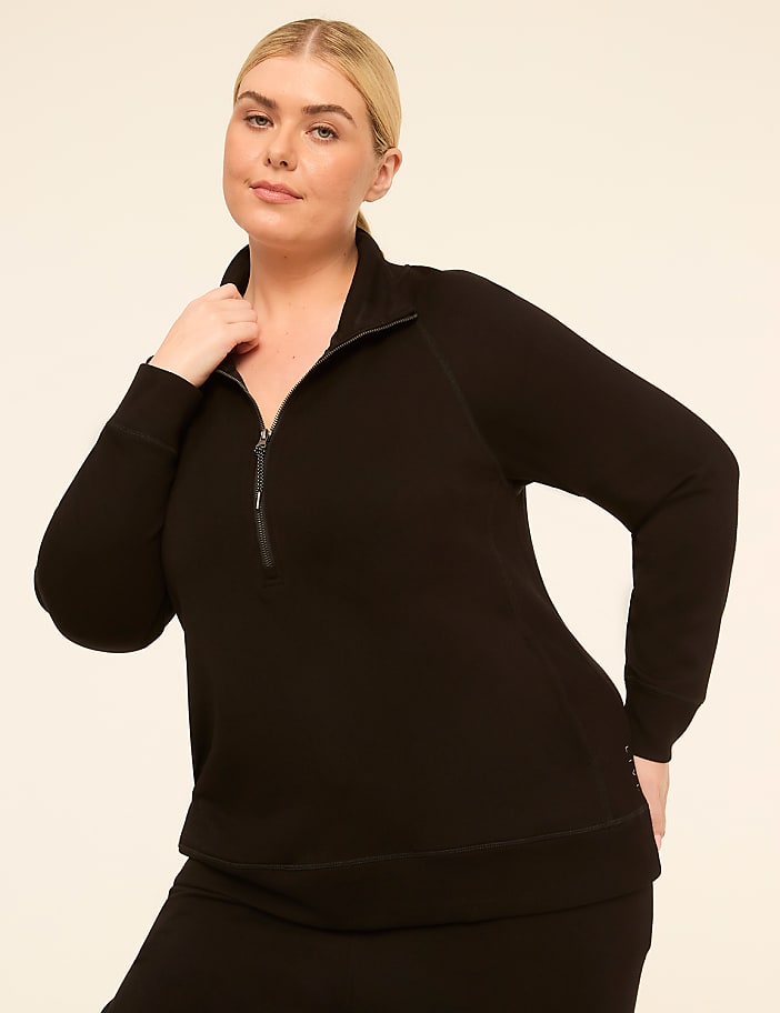A woman in a black quarter-zip sweatshirt stands against a plain, light-colored background.
