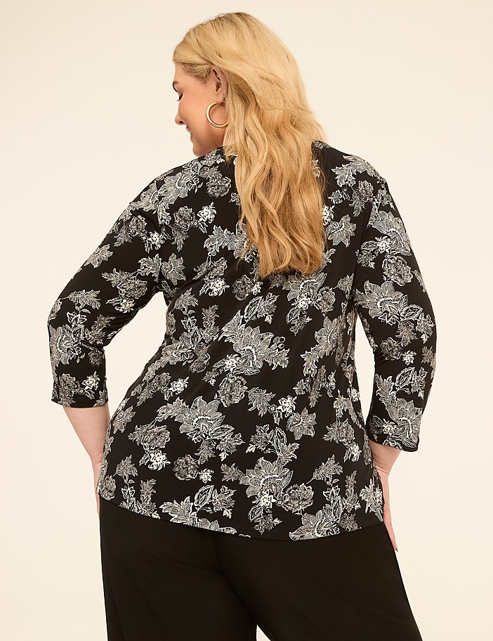 A woman in a black and white floral top stands against a plain, light-colored background.