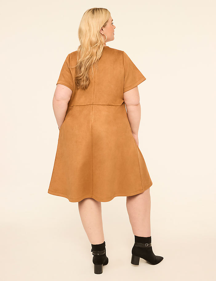 A woman in a tan suede dress and black boots stands against a plain, light background.