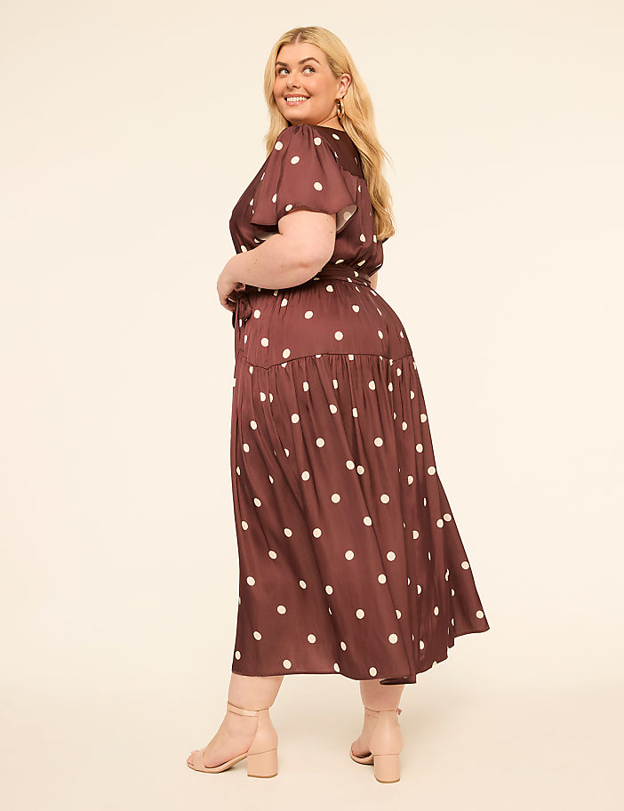 A woman in a polka-dot dress poses against a plain, light-colored background.