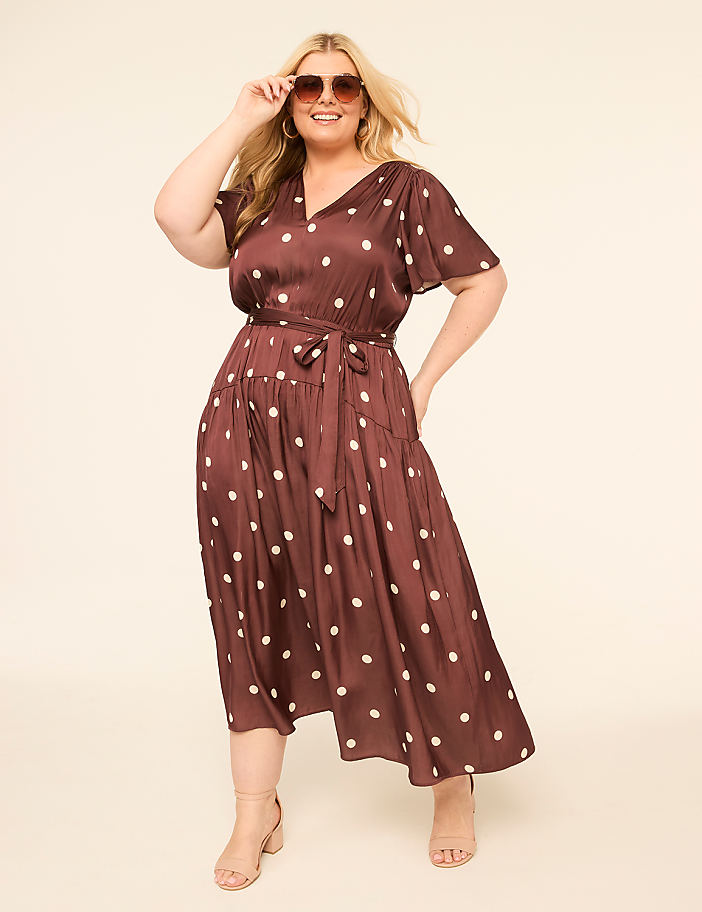 A smiling woman in a polka-dot dress poses against a plain, light-colored background.