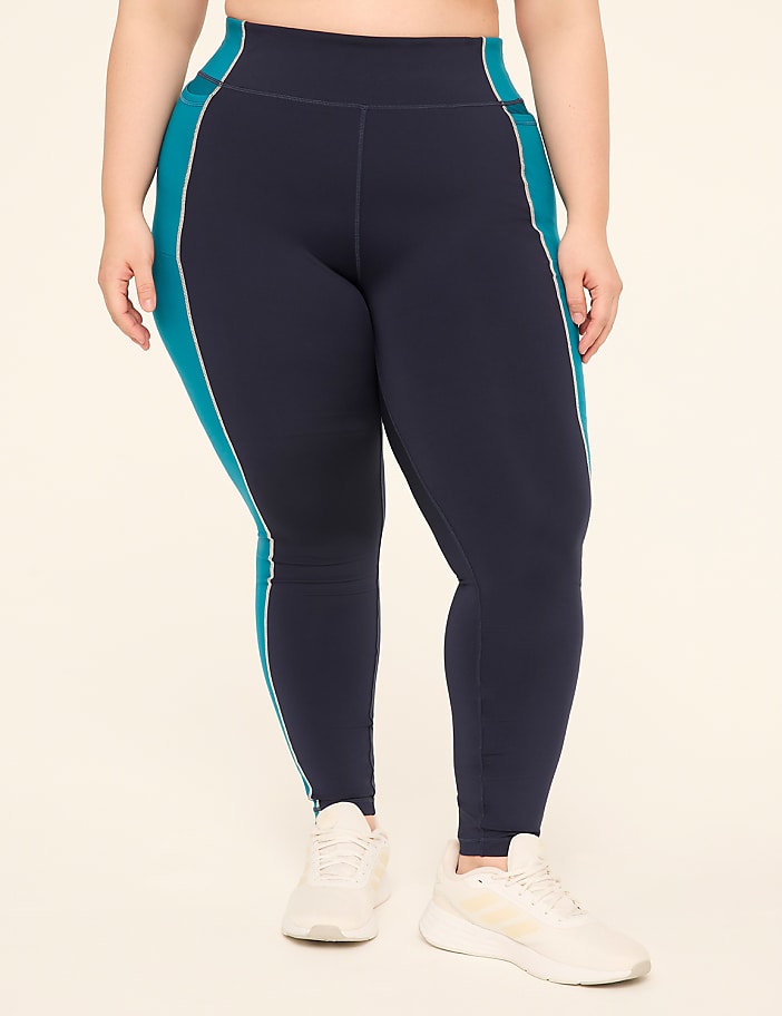 A person wearing navy blue leggings with teal and white side stripes stands on a plain, light-colored background.