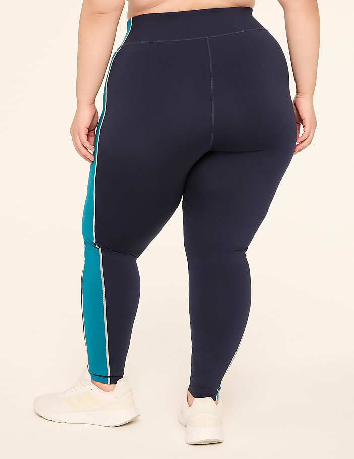 A person wearing navy blue leggings with teal stripes stands on a plain, light-colored background.