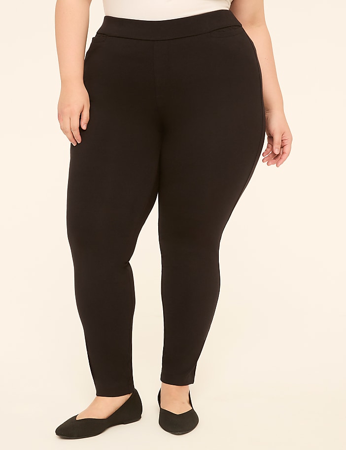 A person wearing black leggings and black ballet flats stands against a plain, light-colored background.