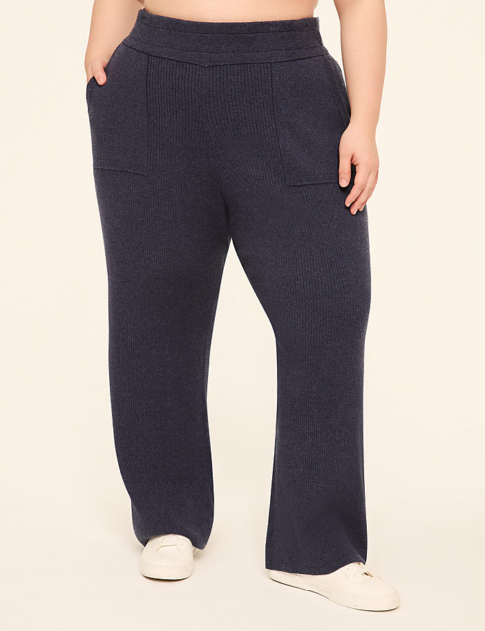 A person wearing navy ribbed knit pants with white sneakers stands against a plain cream background.