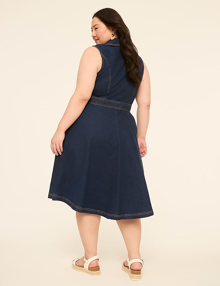 A woman in a denim dress stands against a plain, light-colored background.