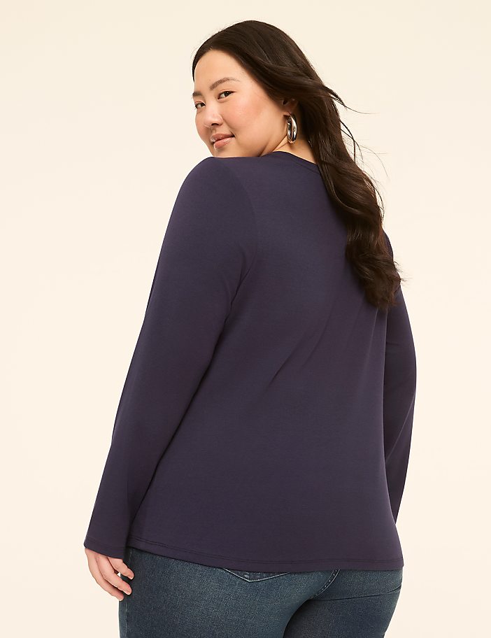 A woman in a navy long-sleeved shirt and jeans poses against a plain, light-colored background.