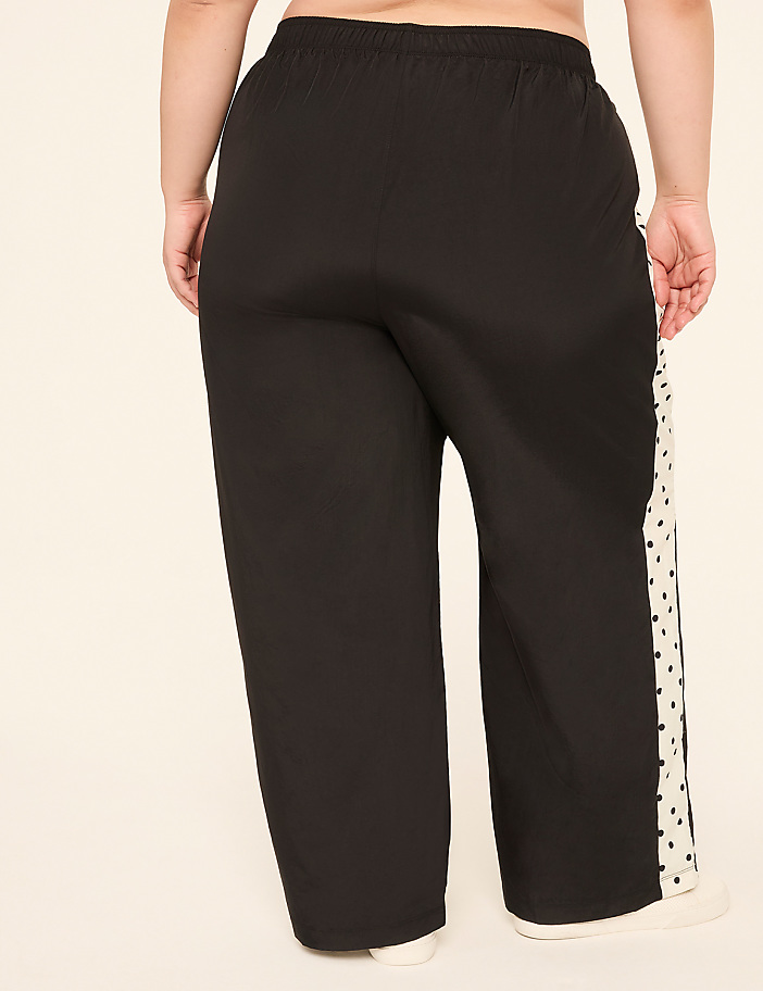 A person wearing black wide-leg pants with a white polka dot stripe down the side stands against a plain, light-colored background.
