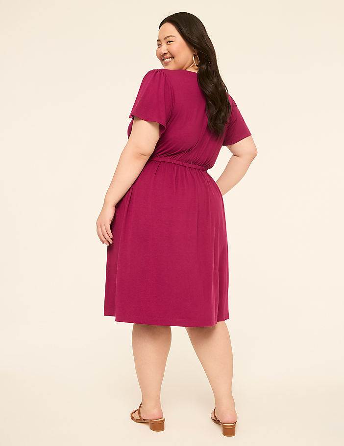 A woman in a magenta dress stands against a plain, light-colored background.
