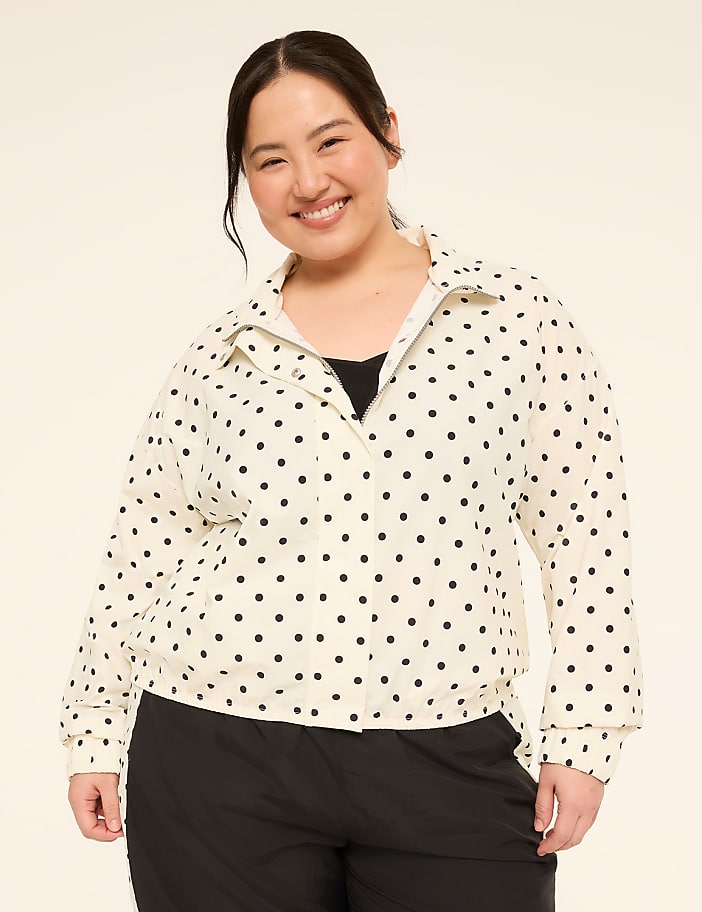 A smiling woman in a polka dot jacket stands against a plain, light-colored background.