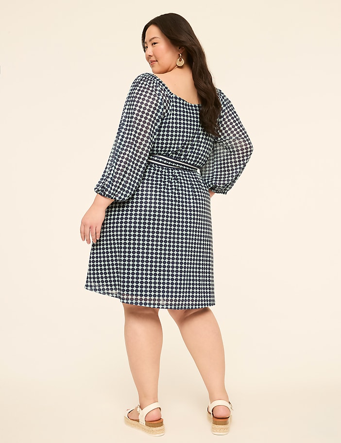 A woman in a blue gingham dress stands against a plain, light-colored background.