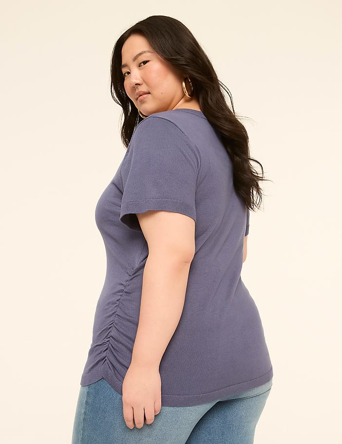 A woman in a blue t-shirt and jeans stands against a plain, light-colored background.