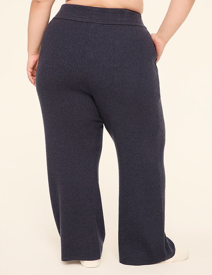 A person wearing dark blue ribbed knit pants stands against a plain, light-colored background.
